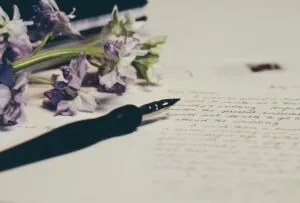 Stylo plume posé sur une lettre manuscrite de condoléances à côté de fleurs séchées violets