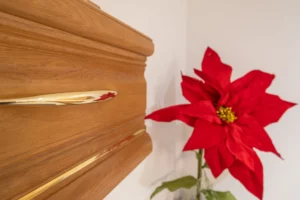 Gros plan sur la poignée dorée d'un cercueil en bois massif à côté d'une fleur rouge décorative